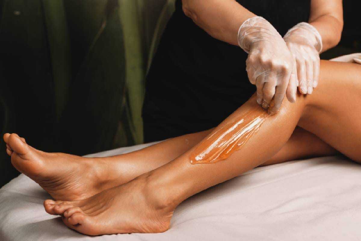 Beautician applying wax to client's leg during a hair removal treatment.
