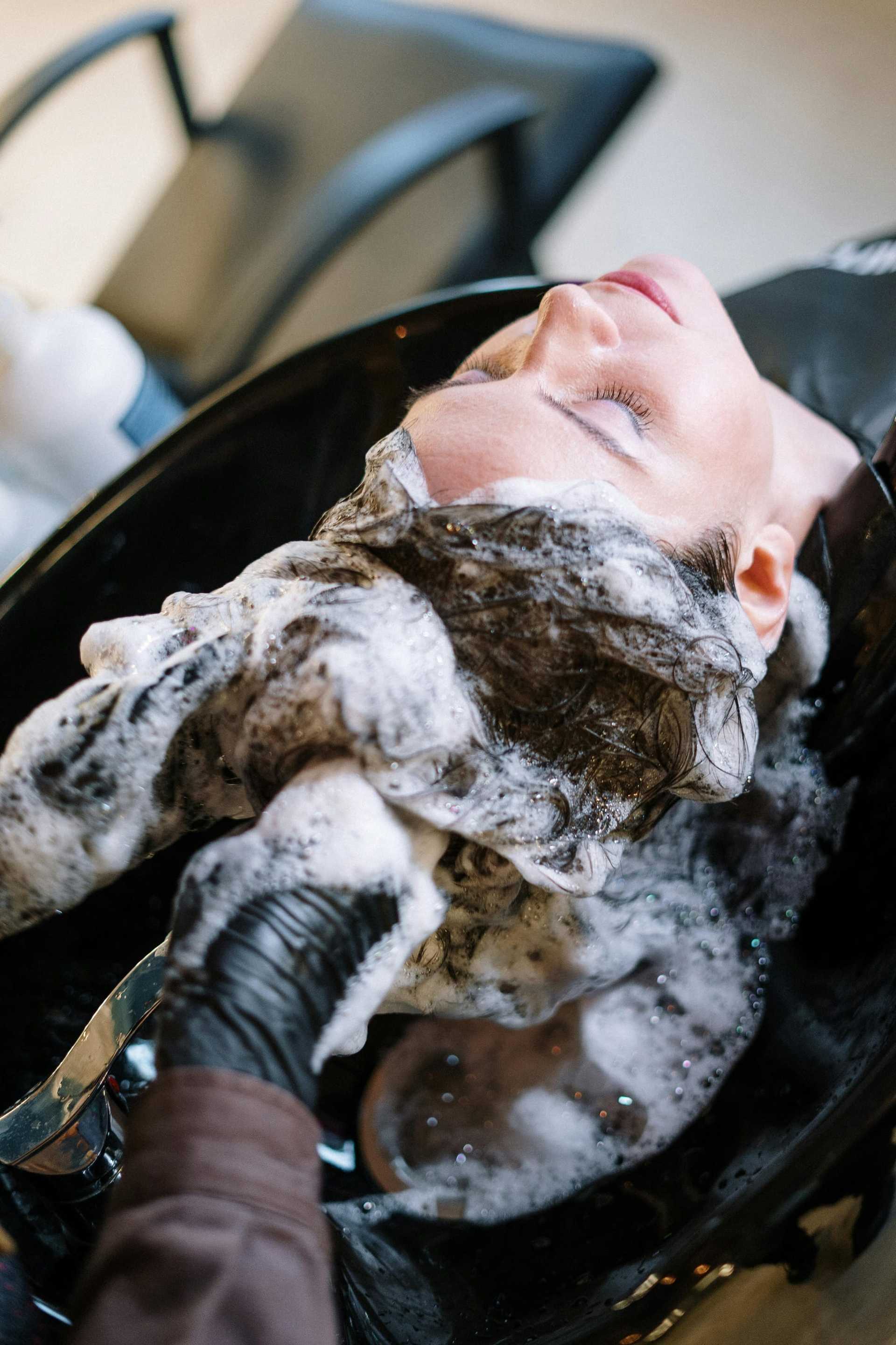 Person getting hair washed at a salon with foamy shampoo.