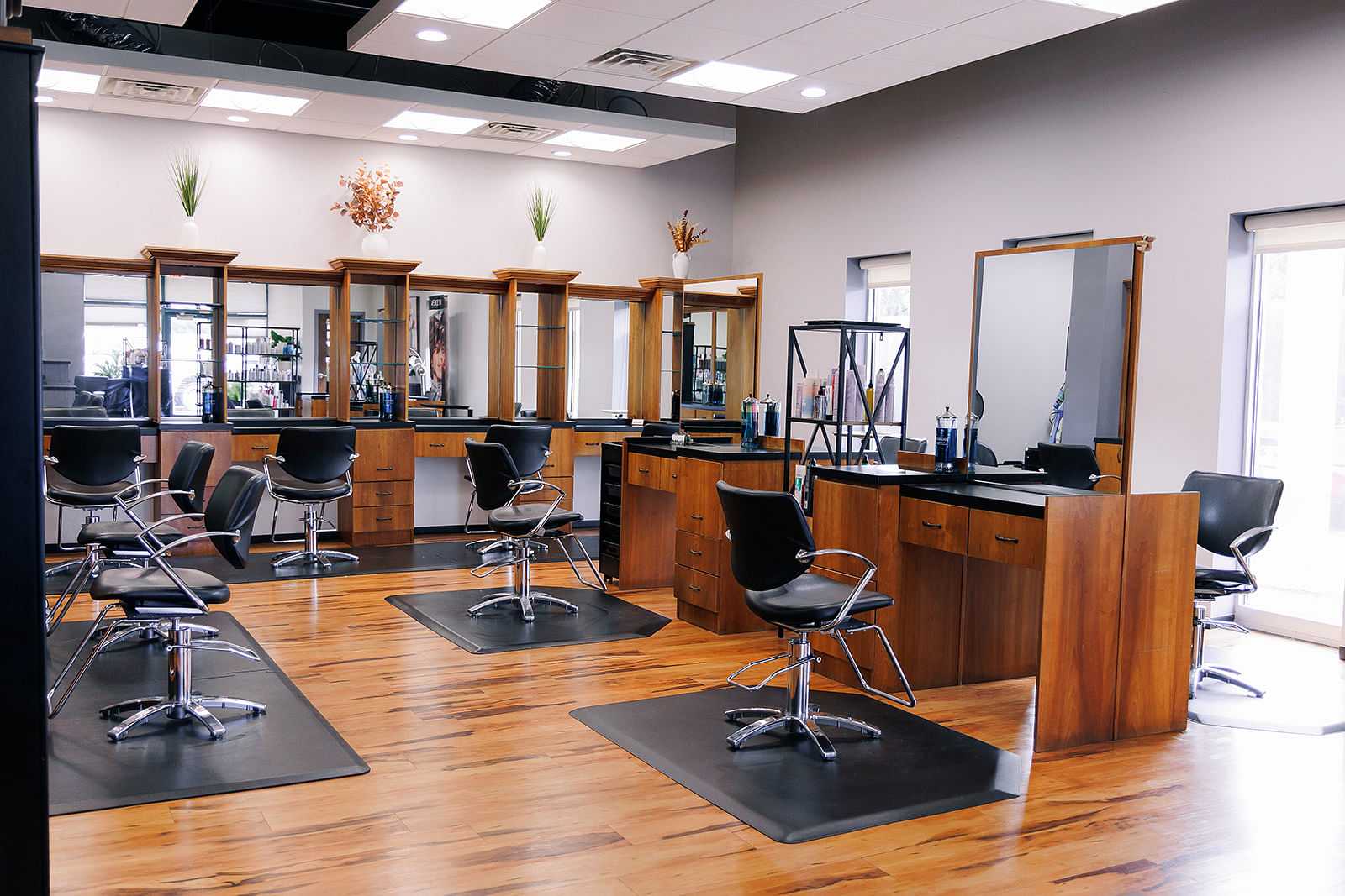 Modern hair salon with wooden stations, black chairs, and large mirrors on a hardwood floor.